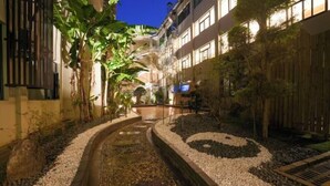 A nighttime view of a hotel courtyard with a water feature, surrounded by plants and a wooden fence. - Yandang Hotel (Wenzhou Teacher Education Institute Yandang) (Yueqing)