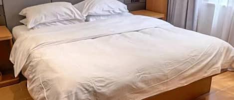 A neatly made bed with white linens in a hotel room with a wooden headboard and a nightstand.