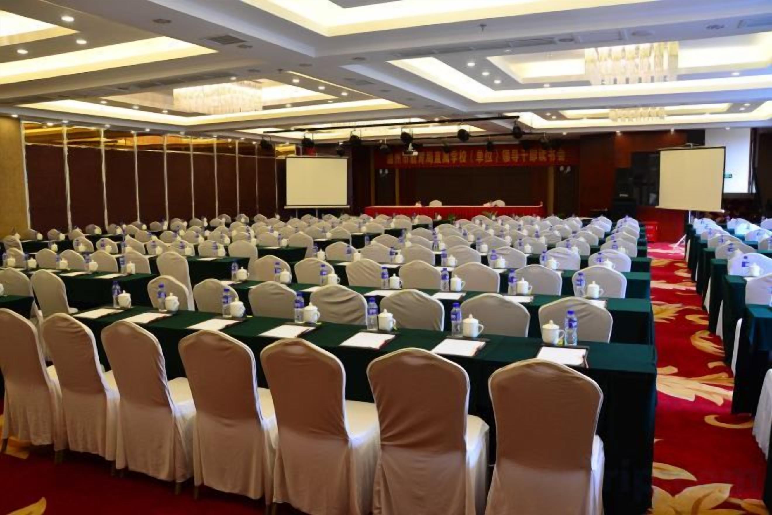 A conference room with rows of tables, chairs, and a projector screen.