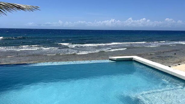 A swimming pool with a view of the ocean and a rocky shoreline. - The Whole Hibiscus - Pool & Ocean Front! (Utila)