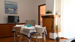 Un comedor con una mesa dispuesta para dos, un televisor sobre un mueble, un radiador y vistas al exterior.