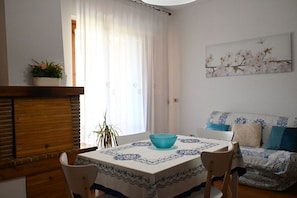 A dining area with a table, chairs, a bowl, a plant, and a sofa with patterned cushions.