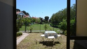 Vista a través de una ventana de un patio trasero con una mesa y sillas, césped y casas al fondo.