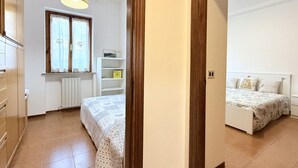 Un dormitorio con cama, una ventana con cortinas, un radiador y una estantería con objetos.