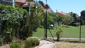 Un quartier résidentiel avec un chemin menant à une entrée fermée par un portail, entouré de verdure et de maisons aux toits recouverts de tuiles rouges.