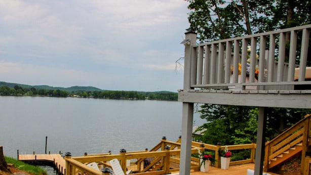 A wooden deck with lounge chairs and a staircase leading to a covered area overlooking a lake.