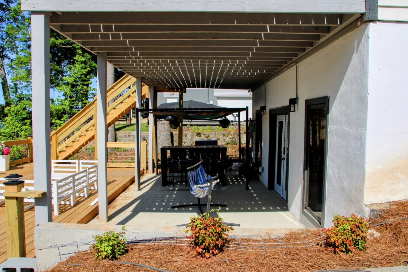 A covered patio area with a barbecue setup, a wooden deck, and a staircase leading to a higher level.