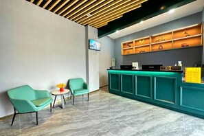 A reception area with teal chairs, a small table, and a reception desk with a TV above it. - Hotel Apartment (Shanghai National Convention and Exhibition Center Jiangqiao Old Street Branch) (Shanghai)