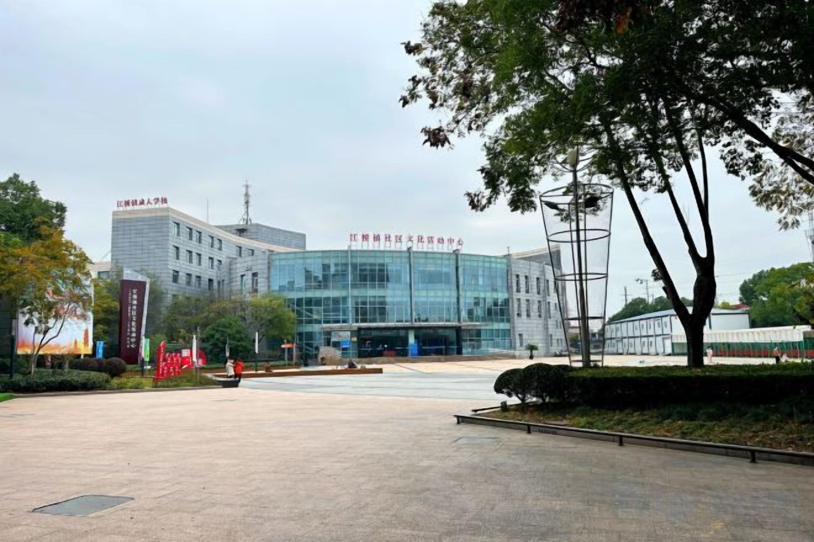 A modern building with a glass facade, a large open plaza, and a few trees.