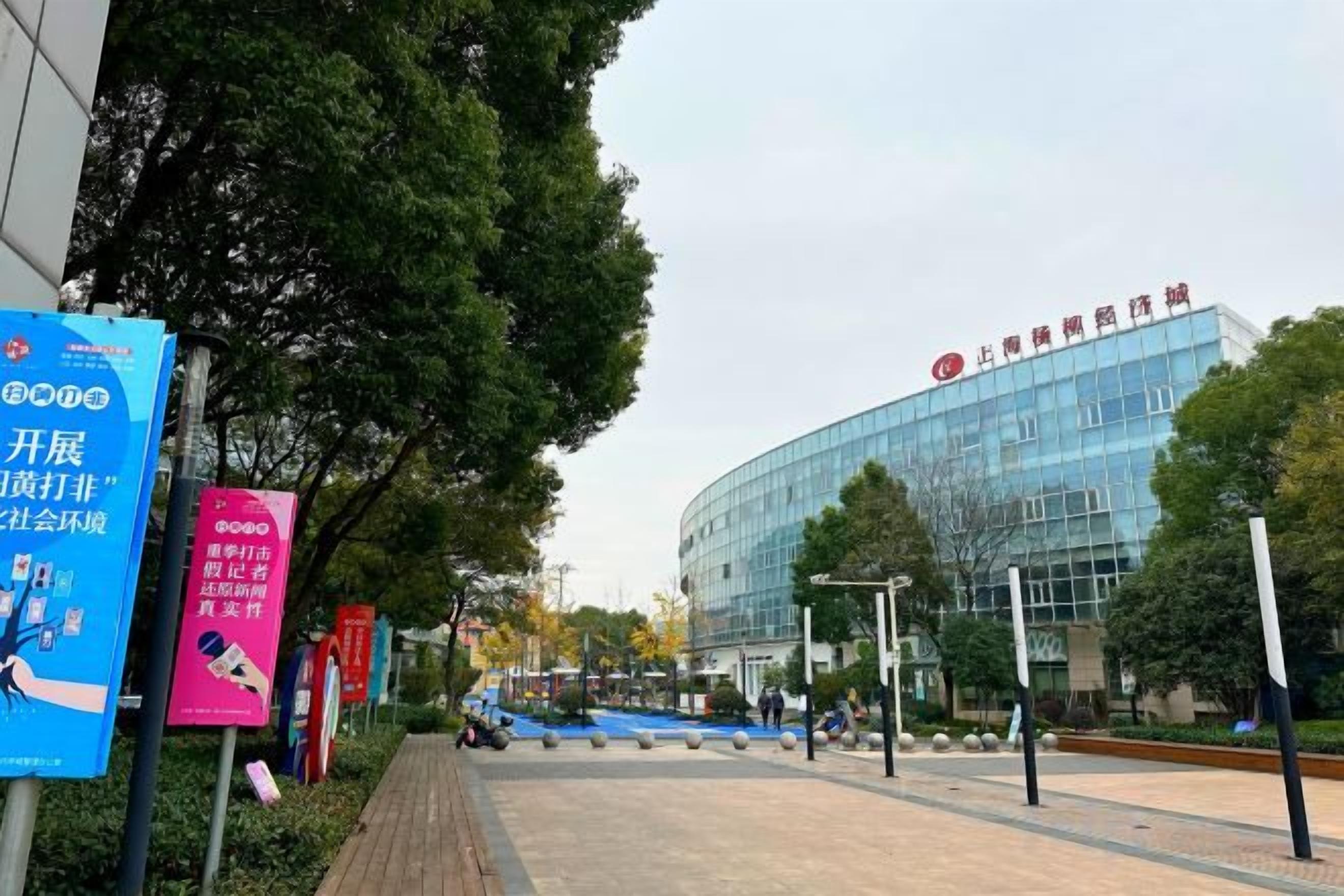 A modern building with a curved glass facade, surrounded by a landscaped area with trees and a paved walkway.