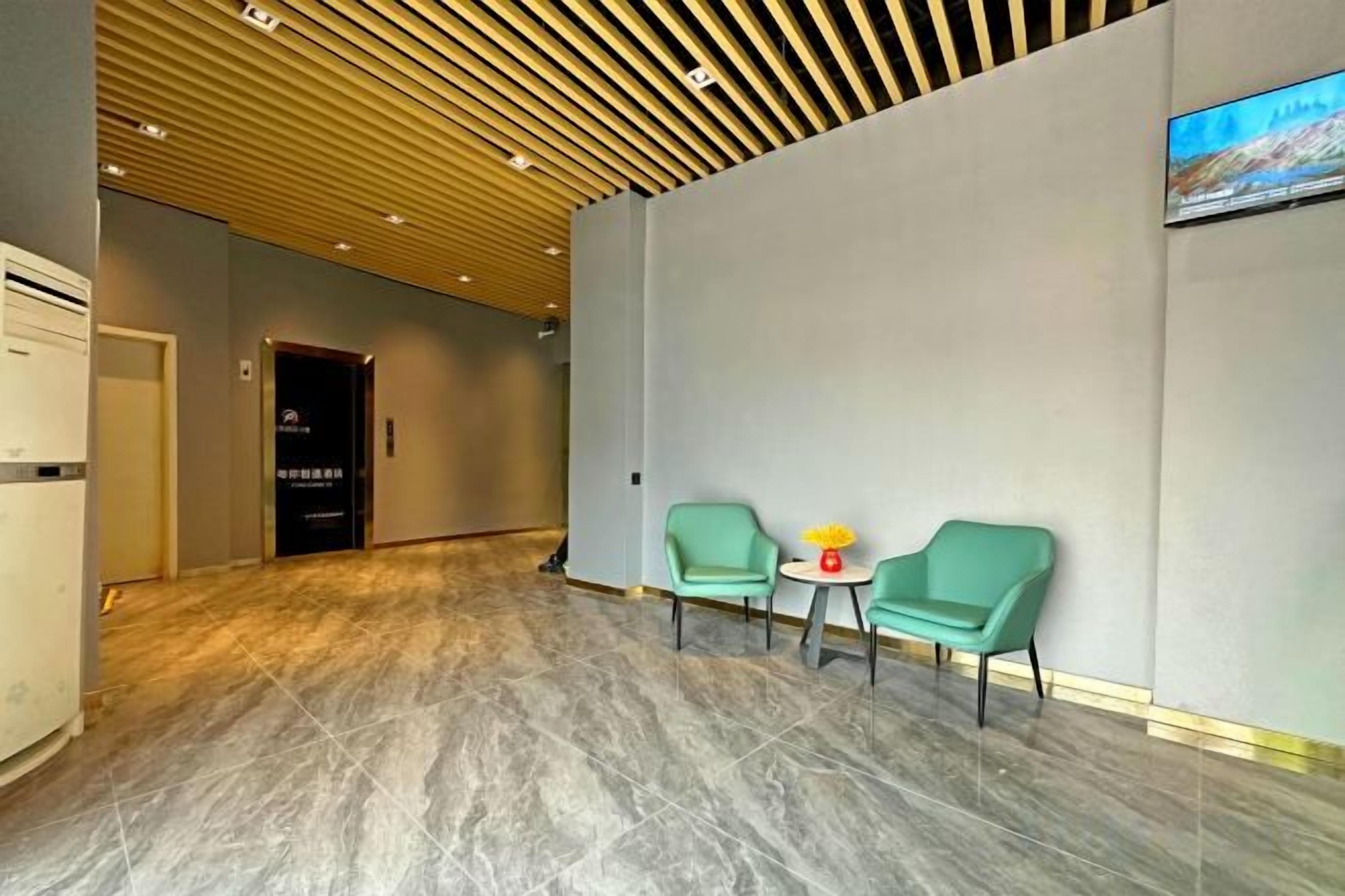 Um hall de hotel com teto de madeira, balcão de recepção e duas cadeiras verdes com uma mesa pequena.