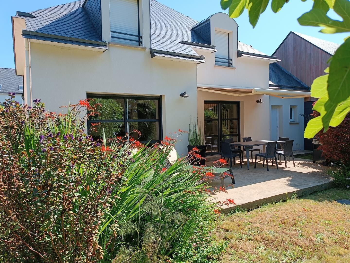 A modern house with a patio, large windows, and a garden with various plants.