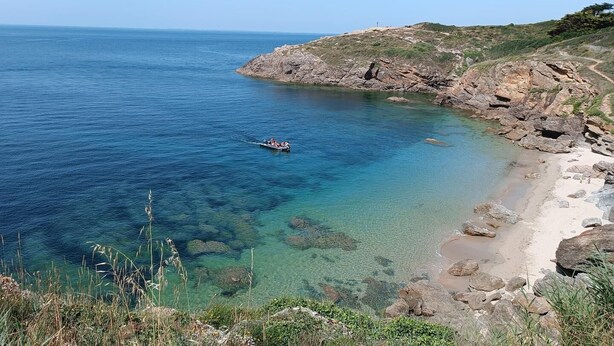 Un paisaje costero con aguas cristalinas, una playa rocosa y un barco a lo lejos.