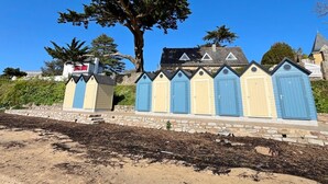 Una hilera de cabañas de playa con un muro de piedra al frente y un árbol grande al fondo.
