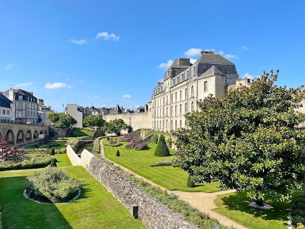 A historic building with a stone wall and a well-maintained garden with pathways and trees.