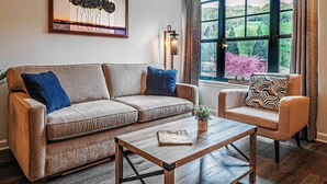 A living room with a sofa, armchair, and coffee table. There is a window with a view of greenery and a painting on the wall. - Condo at Mtn Creek  sleep 4 Mountain view 1 Bdr 1 Bath #234 (Vernon Township)