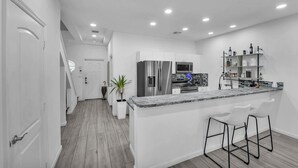 Une cuisine moderne dotée d’un plan de travail en marbre, d’appareils électroménagers en acier inoxydable et d’un coin bar avec des tabourets.