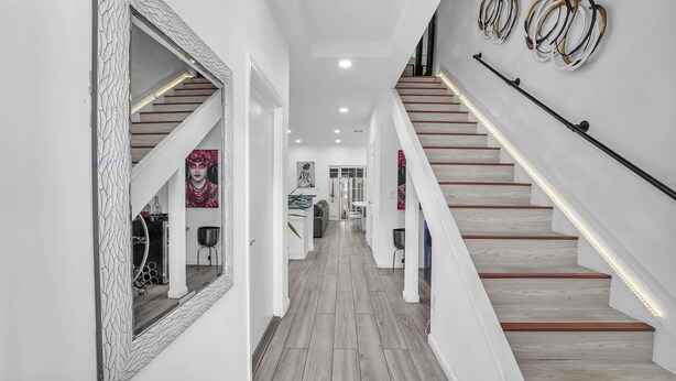 Un intérieur moderne avec un escalier en bois, des murs blancs et un couloir menant à une cuisine.