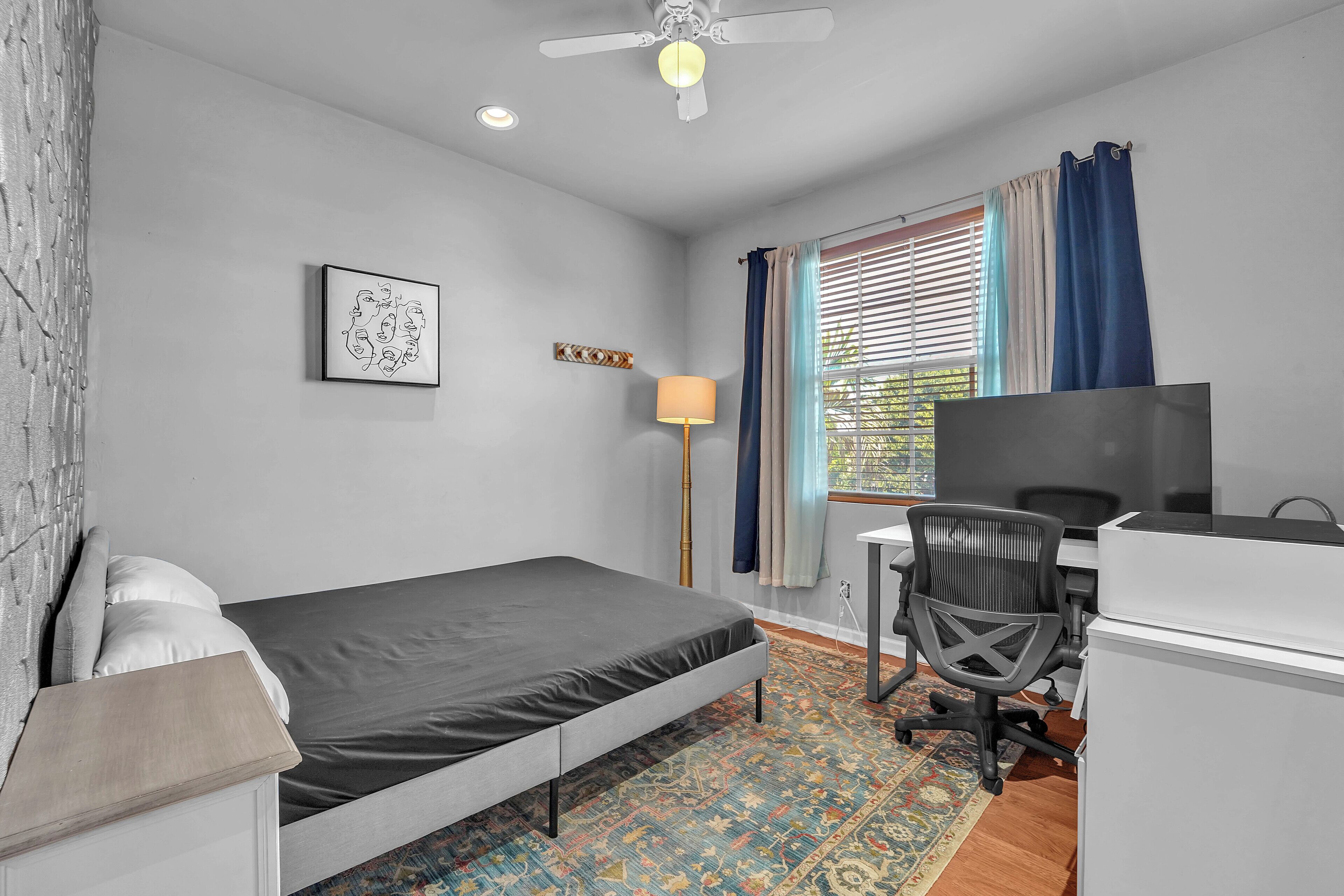 A bedroom with a bed, desk, chair, and a window with curtains.