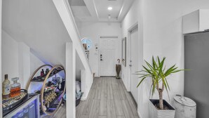 Un couloir avec un plancher en bois, une plante en pot, une poubelle en marbre et une porte blanche.