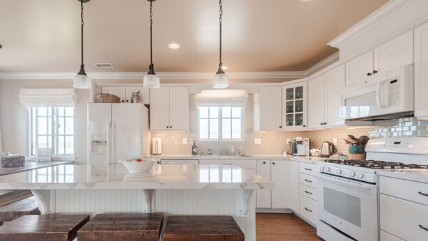 A spacious kitchen with white cabinetry, a large island with stools, a stove, and a microwave.