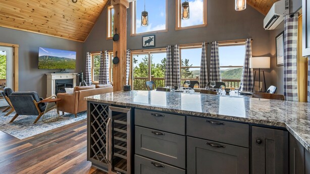 A spacious kitchen with a large island, wooden ceiling, and large windows offering scenic views.