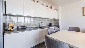 Une cuisine moderne avec des meubles blancs, un pare-feu gris et un coin repas doté de chaises grises recouvertes de tissu.