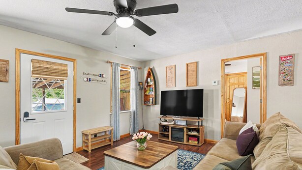 Una sala de estar con ventilador de techo, televisor de pantalla plana, una mesa de centro de madera y un sofá color beige.
