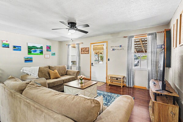 A living room with a ceiling fan, a sofa set, a coffee table, and a television on a wooden stand.