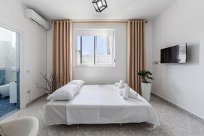 Een hotelkamer met een bed, een televisie, een raam met gordijnen, een kamerplant en uitzicht op het strand.