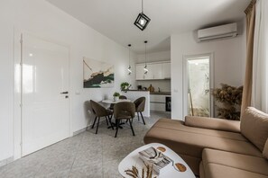 A modern living room with a sofa, a dining table with chairs, and a kitchen in the background.