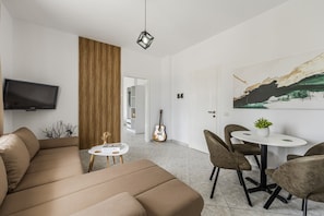 A modern living room with a sofa, a dining table with chairs, a guitar, a TV, and a painting on the wall.