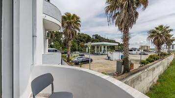 Un balcon avec une chaise, un parking rempli de voitures et, au loin, une station-service.