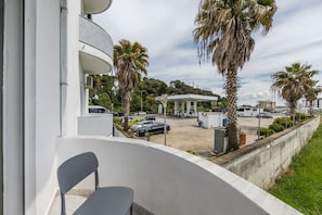 A balcony with a chair, a parking lot with cars, and a gas station in the background.