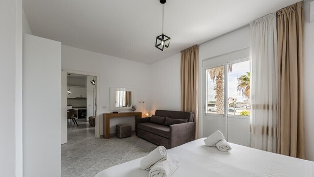 A hotel room with a bed, a sofa, a desk, and a view of the outdoors. - 1BR Apartment with Tree Views | Golem by PikHost (Golem)