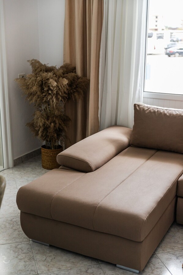 Ein modernes Wohnzimmer mit einer Couch, einem Blumentopf und einem Fenster mit Vorhängen.