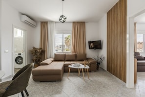 Een moderne woonkamer met een hoekbank, een kleine ronde tafel en een aan de muur bevestigde televisie.