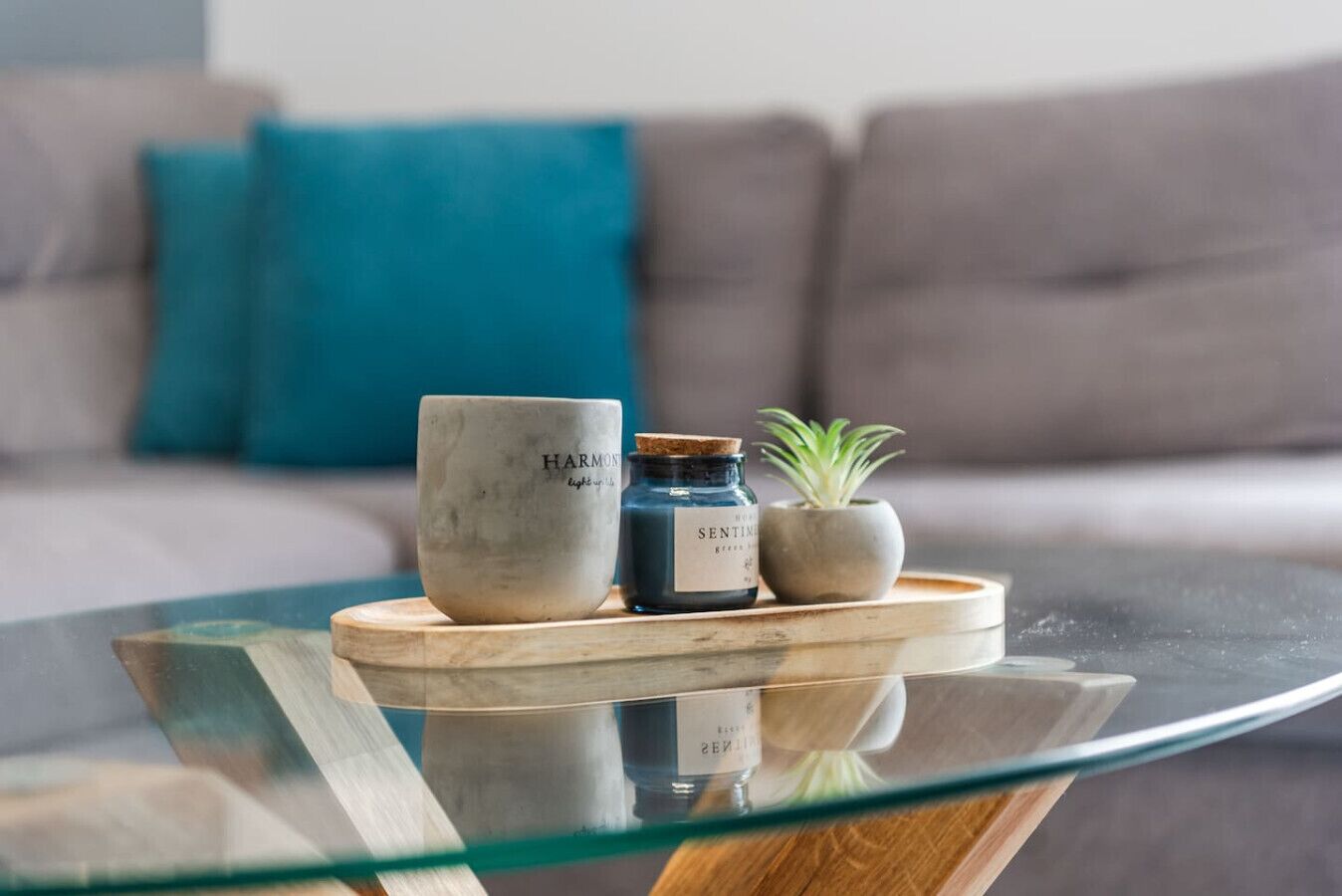 A glass-top table with a ceramic mug, a small blue jar, and a potted plant on a wooden coaster.