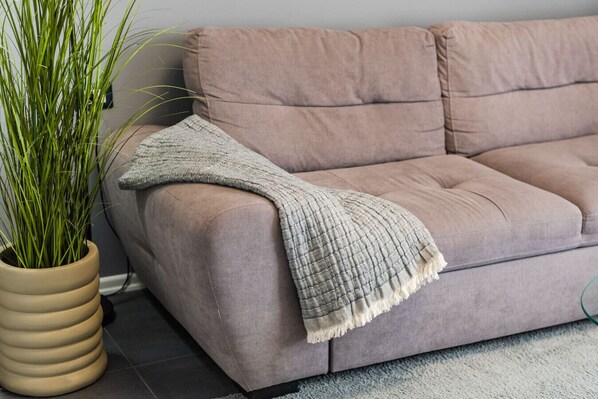 A beige sofa with a textured throw blanket, a potted plant, and a grey carpet.