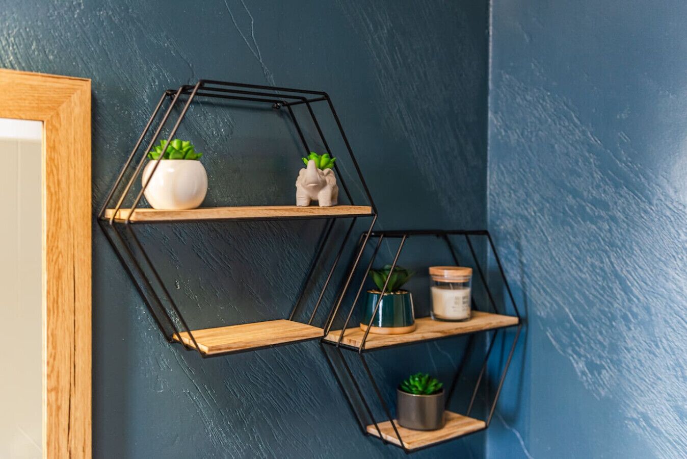 A wall-mounted hexagonal shelf unit with three shelves, each holding various decorative items.