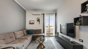 Een moderne woonkamer met een modulaire bank, een glazen salontafel, een flatscreen televisie en een schuifpui naar een balkon.