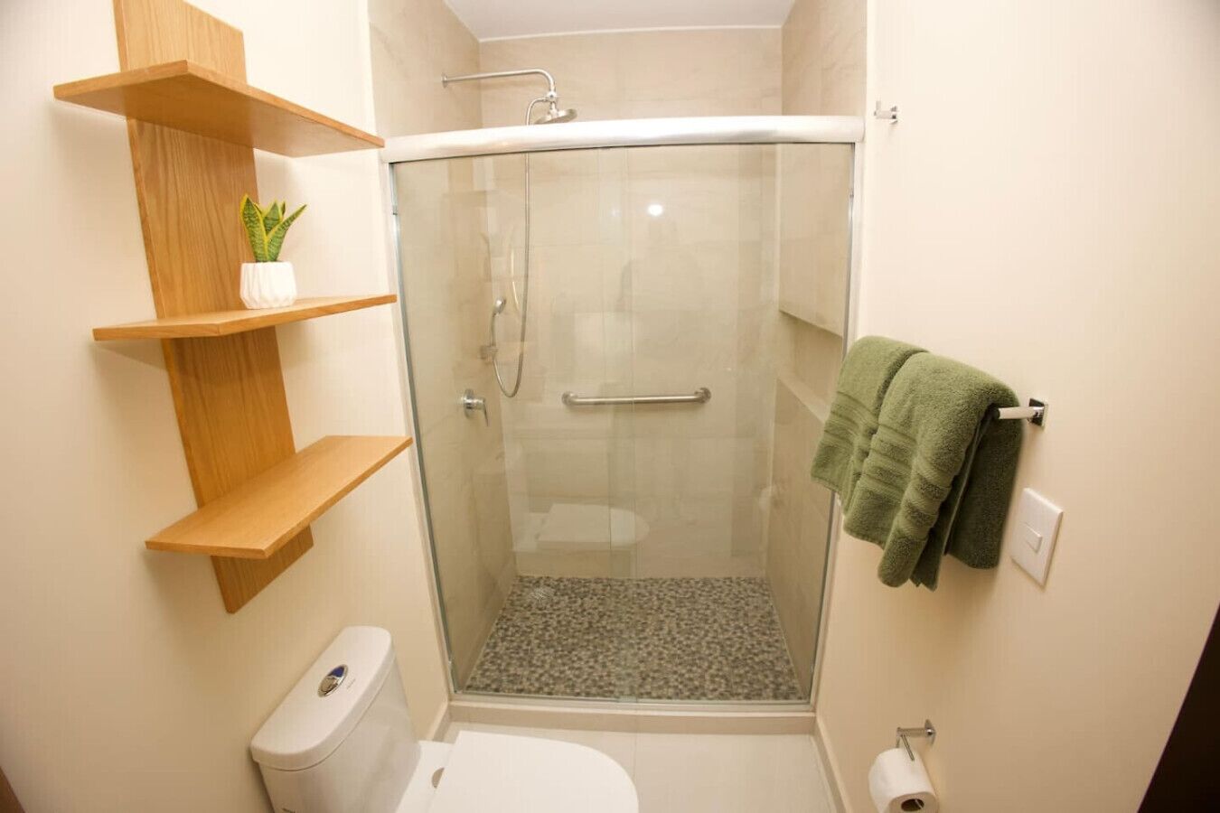 A bathroom with a glass-enclosed shower, wooden shelves, a toilet, and a towel rack.