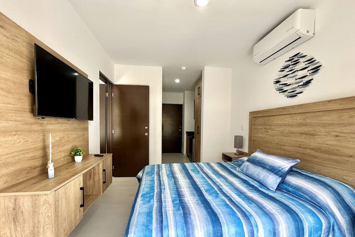 A modern bedroom with a large bed, a TV mounted on a wooden cabinet, and a ceiling fan.