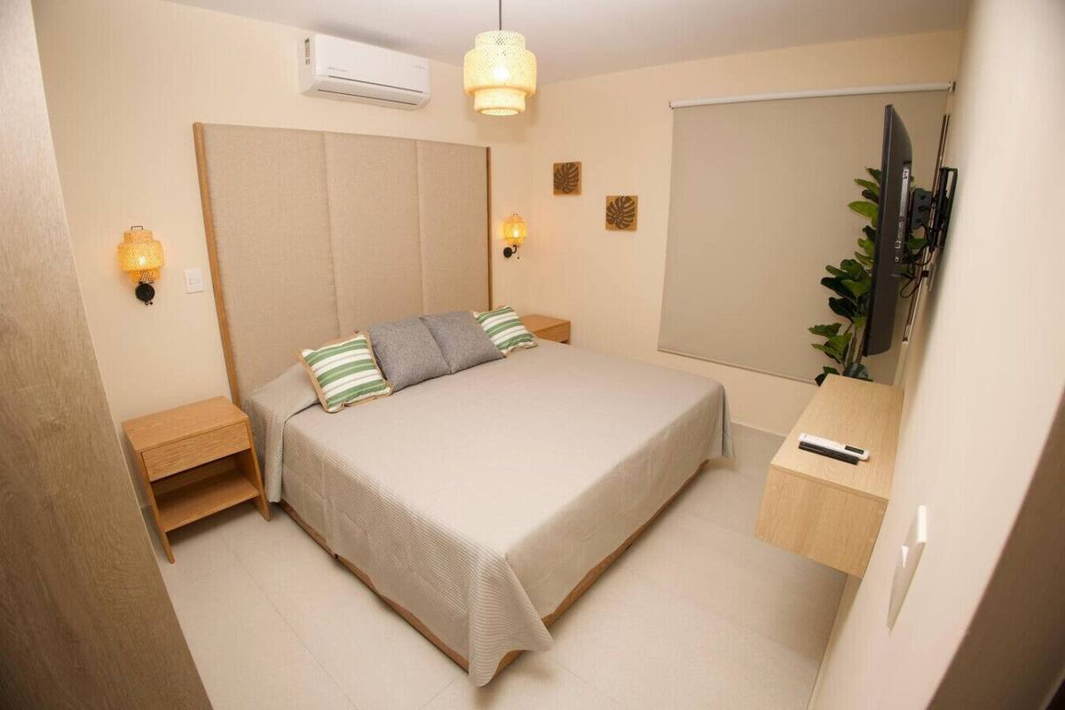 A bedroom with a bed, bedside tables, a TV, and a plant.