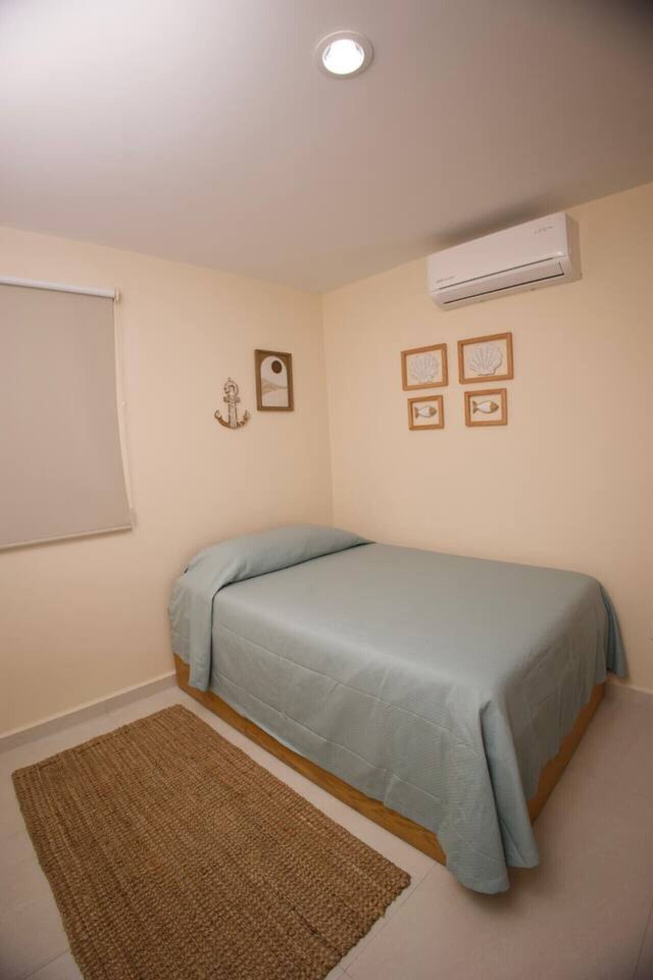 Un dormitorio con una cama individual, una ventana con persiana, aire acondicionado de pared y cuadros enmarcados.