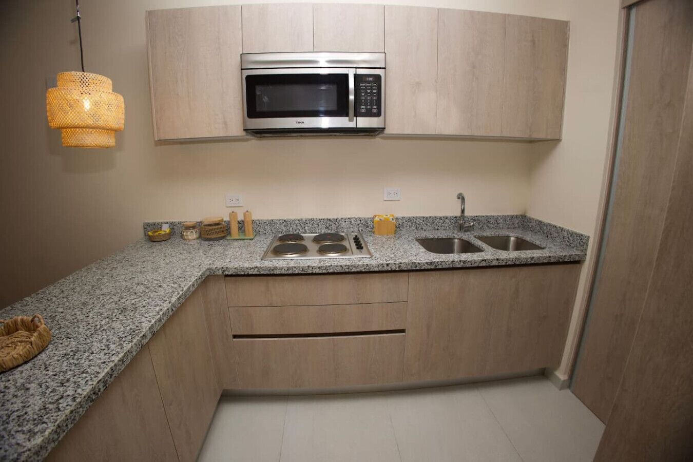 A compact kitchen with a built-in microwave, a granite countertop, a double sink, and wooden cabinetry.