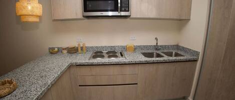 A compact kitchen with a built-in microwave, a granite countertop, a double sink, and wooden cabinetry.