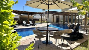 Uma área de piscina com espreguiçadeiras, uma mesa e guarda-sóis.