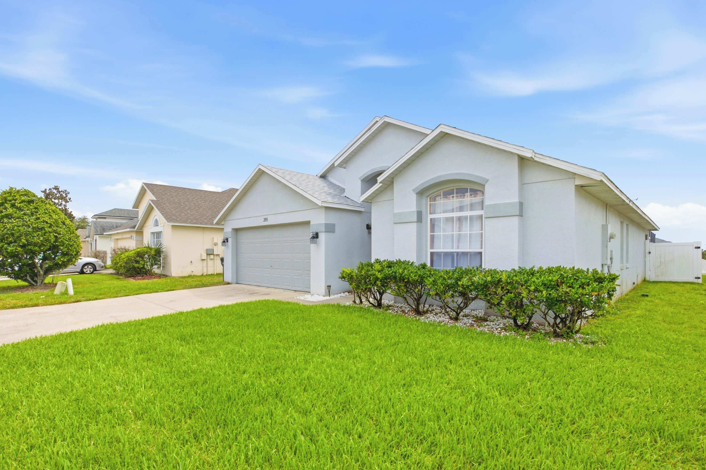 A single-story residential house with a garage, a well-maintained lawn, and a clear sky.