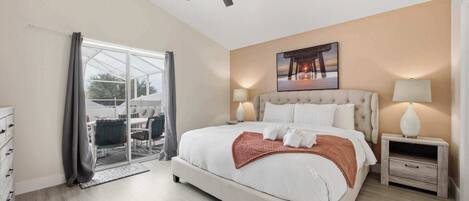 Habitación de hotel con cama, dos mesitas de noche con lámparas, ventilador de techo, ventana grande con cortinas y vista al exterior.